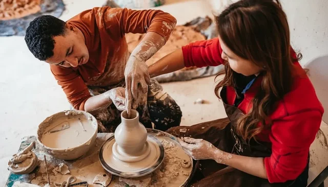 An artisan helping a visitor shape clay on a pottery wheel