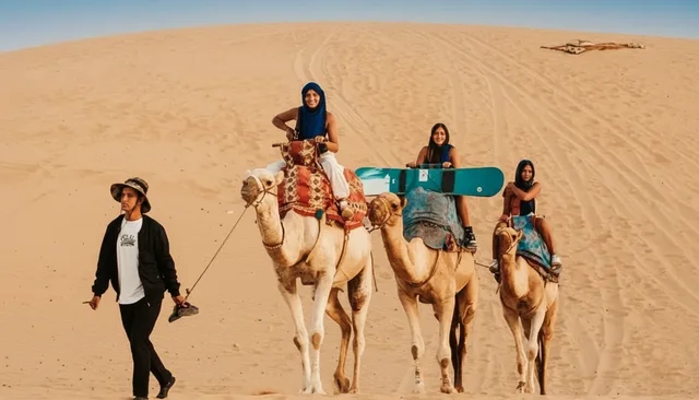 Camel riders accompanied by a guide on the dunes